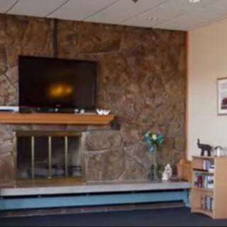 A cozy living room with a television mounted above a fireplace, and a bookshelf to the side.