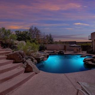 A beautifully lit backyard pool at dusk with stairs leading down to the water.