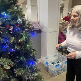A woman decorating a Christmas tree with blue lights and ornaments in a festive setting.