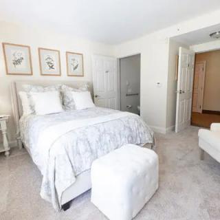 A modern and cozy bedroom with white decor, featuring a bed, artwork on the wall, and comfortable seating.