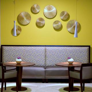 A modern seating area featuring a yellow accent wall with artistic decor pieces and contemporary pendant lighting.