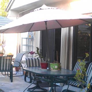 An outdoor patio area with a table, striped chairs, and a large umbrella providing shade.