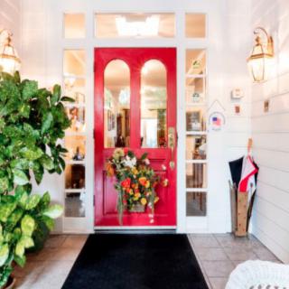A welcoming front entrance with a bright red door adorned with a floral wreath, surrounded by plants and warm lighting.