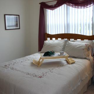 A cozy bedroom with a neatly made bed, featuring a tray on top and bright natural light streaming through the window.