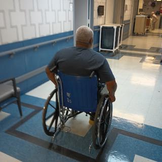 An elderly person in a wheelchair navigating through a hospital corridor.