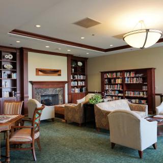 A cozy library lounge with bookshelves, armchairs, and a fireplace.