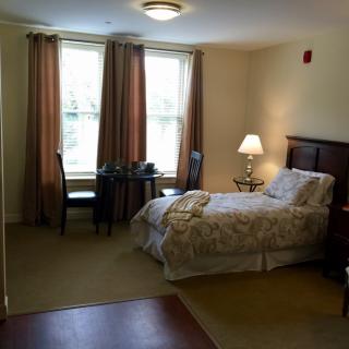 A cozy bedroom with a single bed, table, chair, and lamp near the window.