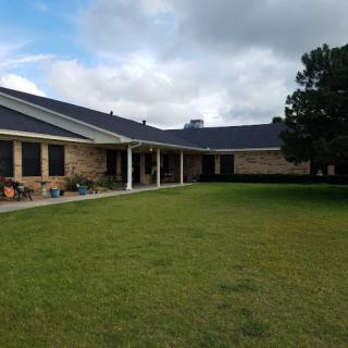 A brick house with a large lawn under a cloudy sky.