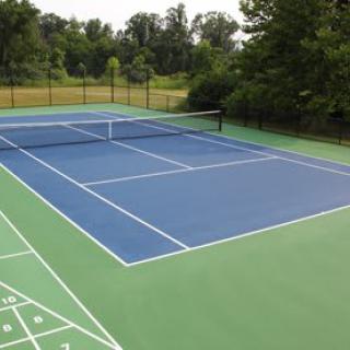 An outdoor tennis court with a blue playing surface and green borders, surrounded by nature.