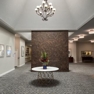 A modern lobby featuring a chandelier, a round table with a flower arrangement, and a prominent brick wall.
