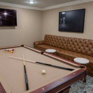 A cozy game room featuring a pool table, leather sofa, and wall-mounted television.