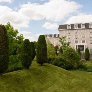 A scenic view of a historic building surrounded by manicured gardens and lush greenery under a partly cloudy sky.