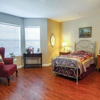 A cozy bedroom with wooden floors, a single bed, and ample natural light from large windows.