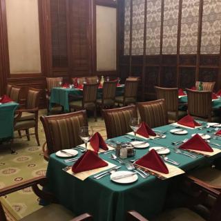 Elegant dining room with tables set for guests, featuring red napkins and green tablecloths.