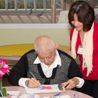An elderly person engaged in painting with the assistance of a caregiver.
