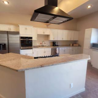A spacious modern kitchen featuring sleek white cabinets, a large island with a granite countertop, and stainless steel appliances.