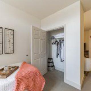 A minimalist bedroom featuring an open closet and a cozy bed with a coral blanket.