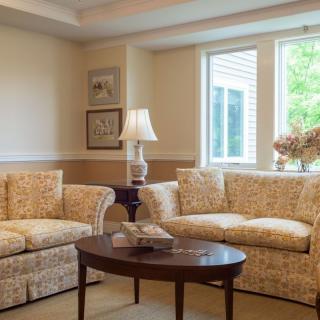 A cozy living room with patterned sofas, a wooden coffee table, and a lamp by the window.
