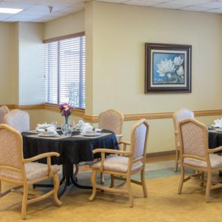 A neatly arranged dining room with tables and chairs set for a meal, featuring wall art and natural light.