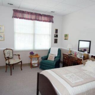 A cozy bedroom interior with a bed, armchair, desk, and window.