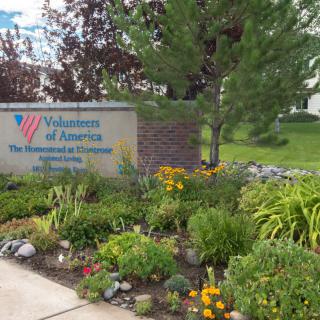 A landscaped garden with a sign for Volunteers of America, featuring colorful flowers and greenery.
