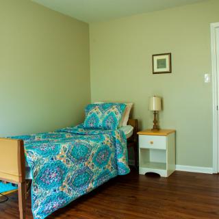 A simple bedroom with a single bed, colorful bedding, and a nightstand with a lamp.