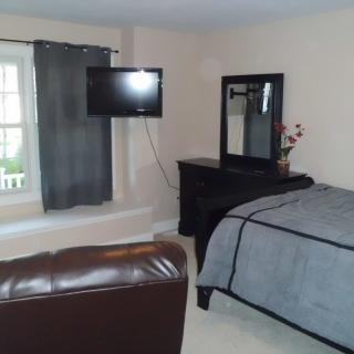 A cozy bedroom featuring a bed, dresser with a mirror, and a wall-mounted television.