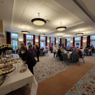 An indoor gathering with people seated at tables and a buffet setup.