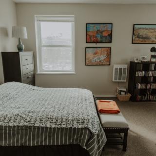 A cozy bedroom with a bed, dresser, lamp, and artwork on the walls.
