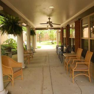 A covered patio with chairs and plants, featuring a ceiling fan.