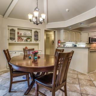 A cozy dining area with a wooden table and chairs, adjacent to an open kitchen, featuring a chandelier overhead.