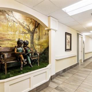 A hallway featuring a sculpture of children on a bench, embedded into the wall with decorative artwork behind it.