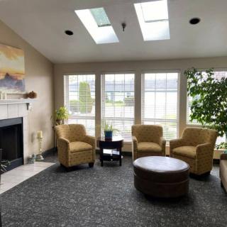 A cozy living room with comfortable chairs, a coffee table, and a fireplace, illuminated by natural light from skylights and large windows.