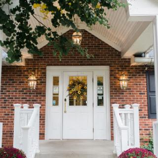 A charming entrance to a home, featuring a welcoming white door, decorative lights, and seasonal wreath.
