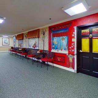 A colorful hallway with decorative wall paintings and a row of red chairs along one side.