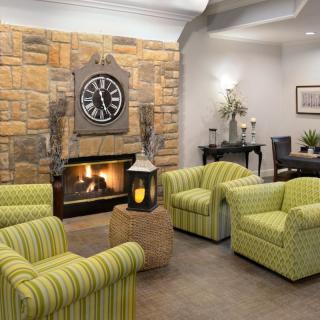 A cozy living room with striped armchairs, a stone fireplace, and a large wall clock.