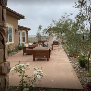 A cozy patio with outdoor seating surrounded by greenery and the exterior of a house.