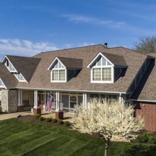 A large, suburban house with a well-maintained lawn and garden under a clear blue sky.