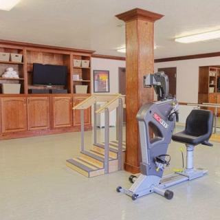 A room equipped with exercise machinery, featuring a bike machine and wooden shelving with a TV.