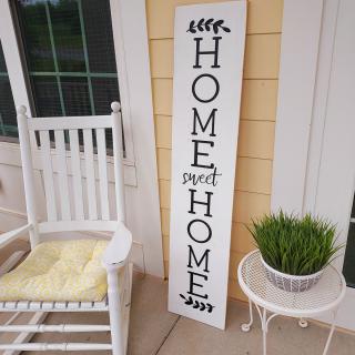 A cozy front porch with a 'Home Sweet Home' sign, a rocking chair, and a potted plant.