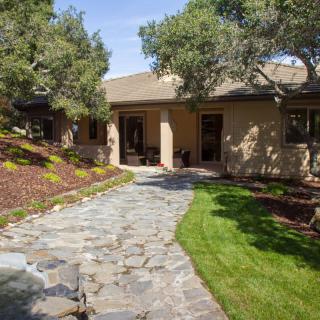 A well-landscaped front yard with a stone pathway leading to a house surrounded by trees and grass.