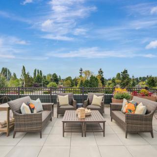 A spacious patio area featuring wicker furniture with cushions, set against a backdrop of a clear blue sky and lush greenery.