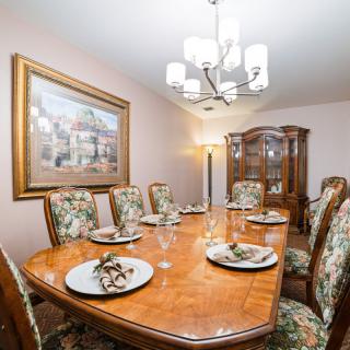 An elegant dining room featuring a large wooden table set with plates and patterned chairs, illuminated by a chandelier.