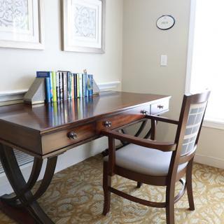A cozy home office space with a wooden desk, books neatly arranged on top, and a comfortable upholstered chair nearby.