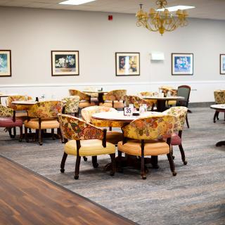 A cozy dining area with multiple tables and patterned chairs, decorated with framed pictures on the walls.