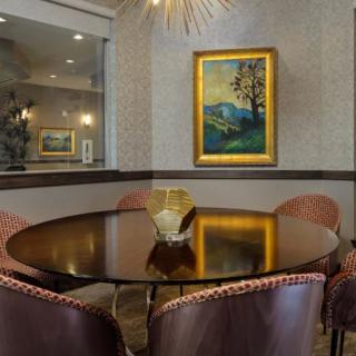 A stylish modern dining area with a round table, upholstered chairs, and a framed painting on the wall.