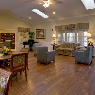 A cozy and well-furnished living room featuring a sofa, chairs, a table, and a piano with ample natural light from the windows.