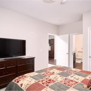 A modern bedroom featuring a TV on a dresser, with a bed covered in a colorful quilt.