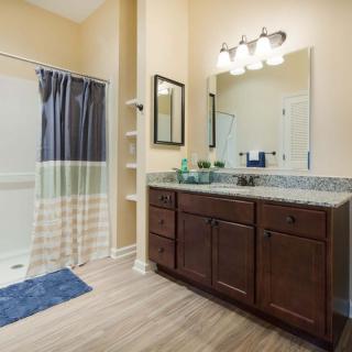 A well-lit bathroom featuring a double sink vanity with wood cabinets and a large mirror, along with a shower area separated by a curtain.
