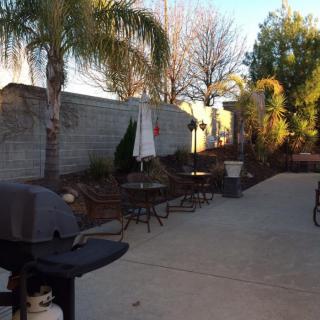 A sunny backyard patio with outdoor furniture and a grill.